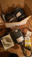 Photo showing three cylindrical A/C motors in a box alongside an electrical regulator, a belt, and other small electrical parts on a wooden floor.