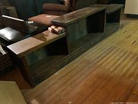 Long rectangular pine wood side storage bench with three open shelf compartments, showing some wear and scratches on the surface.