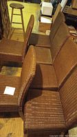 View of six woven reed Parsons style chairs arranged side by side, showing seat and back surfaces with some visible wear.
