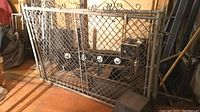 Two metal gates with wire mesh panels leaning against a wall, showing full gates and surroundings.
