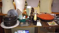 Wide shot showing assortment of kitchenware including cast iron cookware, muffin tins, cookie cutters, pepper mills, platter, and decorative bottle.