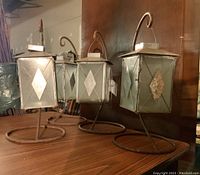 Front angle showing three of the four metal lanterns, highlighting the diamond-pattern etched glass panels and metal frames with curved hangers on round bases.