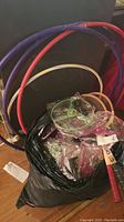 Photo showing 3 hoola hoops in red, purple, and blue, along with a black bag filled with packaged flying spinner toys and some badminton rackets.