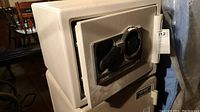 View of the Sentry S029 fire safe showing the door, handle, and combination dial lock on the front surface of the safe. Beige color safe with visible hinges on the right.