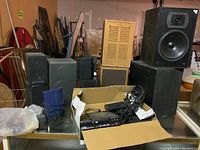 Photo shows various speakers stacked including large black speakers, a wooden speaker, smaller black speakers, and an open box with cables and Diamond DVD player on a glass table.