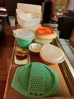 Various sizes of Tupperware food storage bowls and containers stacked on table showing colors white, green, orange, and red, including lids.