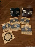 Two View-Master viewers and several View-Master reels on wooden surface.