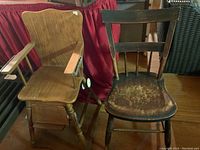 Vintage child's high chair in light wood with curved back, armrests, and stretcher bar next to a dark wooden chair.