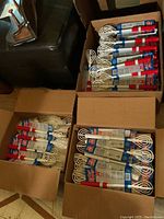 Three boxes filled with multiple white-coated whisks with red and white handles, showing quantity and packaging.