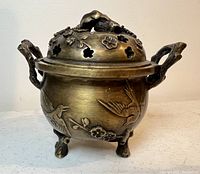 Side view of antique brass coal pot/incense burner showing bird and floral relief decorations, two side handles, and three legs.