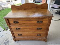 Front view of antique wooden chest of drawers showing three drawers with metal handles and shaped backboard