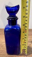Full view of antique cobalt blue glass eye wash bottle with measuring tape showing height approximately 7.5 inches.