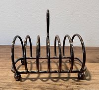 Front view of antique silver plated toast rack with six arches and central handle, placed on wooden surface.