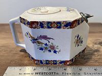 Side view of the antique porcelain teapot showing its octagonal shape, floral decoration, and pewter spout, with ruler for scale.