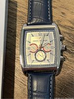 Front view of Daniel Hechter wristwatch showing rectangular beige dial with three subdials and black numerals with blue leather strap.