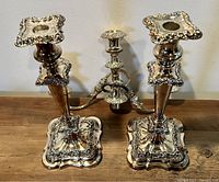 Pair of ornate vintage silverplate candlesticks with square bases and decorative tops shown side by side.