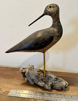 Full side view of the hand carved wood bird decoy on natural driftwood base with ruler for size reference.