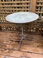 Full view of the vintage cast iron outdoor table showing round top and ornate iron base on wooden deck.