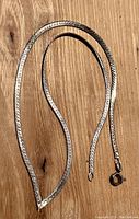 Full view of sterling silver herringbone chain necklace laid on a wood surface, showing the entire length and clasp.