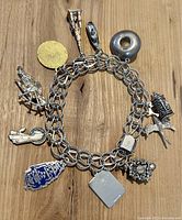Full view of the sterling silver charm bracelet with eleven different charms attached, laid flat on wood surface.