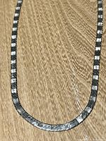 Full view of the sterling silver herringbone chain necklace showing the unique textured pattern on the front surface.