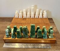 Front view showing the complete chess set with white and green stone pieces arranged on a wooden chessboard with ruler for scale.