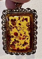 Front close-up of rectangular vintage amber pendant showing amber clarity and floral inclusions.