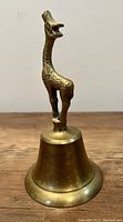Front view of vintage brass bell showing giraffe handle attached to brass bell base on wooden surface.