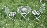 Full view of vintage cast iron bistro set with round table and two chairs on grass.