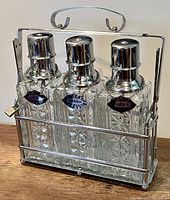 Front and side view of 3 bottle liquor set tantalus with chrome tops, cut glass bottles marked Bourbon, Vodka, and Gin.