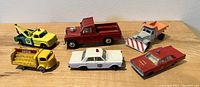 Full lot of six vintage toy cars and trucks arranged on a wooden surface showing the variety and condition.