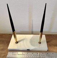 Front view of marble base with two black pens in gold tone holders, ruler included for scale approximately 6.5-7 inch wide base