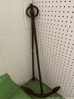 Photo showing entire antique metal anchor hook standing upright against wall, showing stock and shank with rust patina.