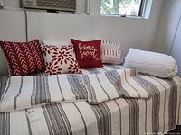 Twin size bed with striped black and white coverlet, four decorative throw pillows in red, white, beige, and body pillow on right side.