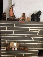 Overview of grouped decorative items arranged on a stone fireplace mantel including a copper and driftwood sailboat model, various African-style wooden figurines, elephant figurines, and small decorative boxes