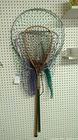 Three vintage fishing nets displayed hanging on pegboard: two with aluminum frames and green nets, one with wooden frame and natural fiber net.