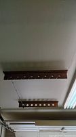 Two dark wooden fishing pole hangers mounted horizontally on the ceiling, one with round holes for handles, one with hooks for securing rods. One fishing rod hanging from the hook hanger.