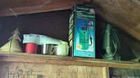 Shelf showing Green Thumb garden sprayer in original box, plastic funnels, and measuring cups.