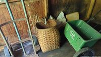 Photo showing metal hand truck, green garden spreader, and woven fish basket inside shed