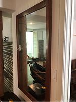 Front view of large rectangular mirror with solid wood frame hung on wall reflecting interior room.