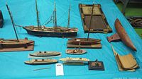 Wide view of all model ships on blue sheet, including schooners, fishing boat, cruise ships, ship frame, and boat bottom