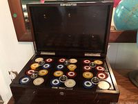 Open wooden glossy box displaying arranged poker chips in four colors with suit symbols.