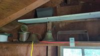 Large antique brass ship's horn and two brass bells on a wooden shelf under eaves of a shed