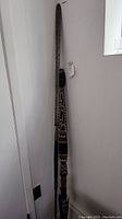 Full view of the wooden carved and painted tribal spear leaning against a wall, showing the intricate painted and carved details along its length.
