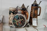 Three vintage ceramic steins and one ceramic flask displayed on a shelf. Two steins have metal lids, one stein is missing a lid. Flask has a painted hunting scene.