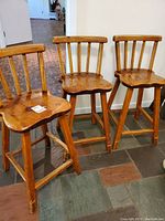 Three vintage wooden stools with peg joinery, visible wear, and contoured seats arranged together.