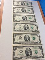 Six US two-dollar bills laid out in a row, front side visible showing portraits of Thomas Jefferson and green seals.