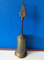Full view of the brass fireplace brush with ship handle against a blue background
