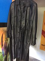 Full view of black leather long coat hanging, showing length and overall condition.