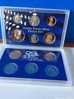 Close-up view of two plastic cases showing 2004 US Mint Proof Set coins including Roosevelt dime, Jefferson nickel, Lincoln penny, Kennedy half dollar, Washington quarter and 5 State Quarters.